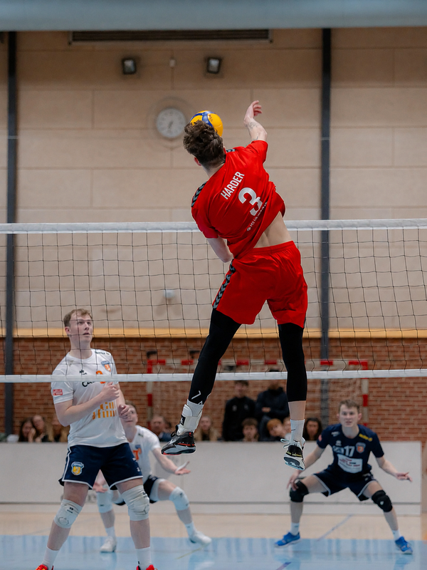 Volleyballspiller i rød trøje springer og spiker bolden over nettet